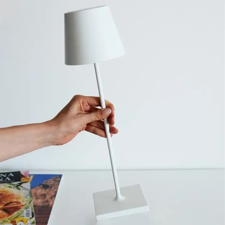 Hand adjusting a white lamp on a light gray surface with a magazine in the background