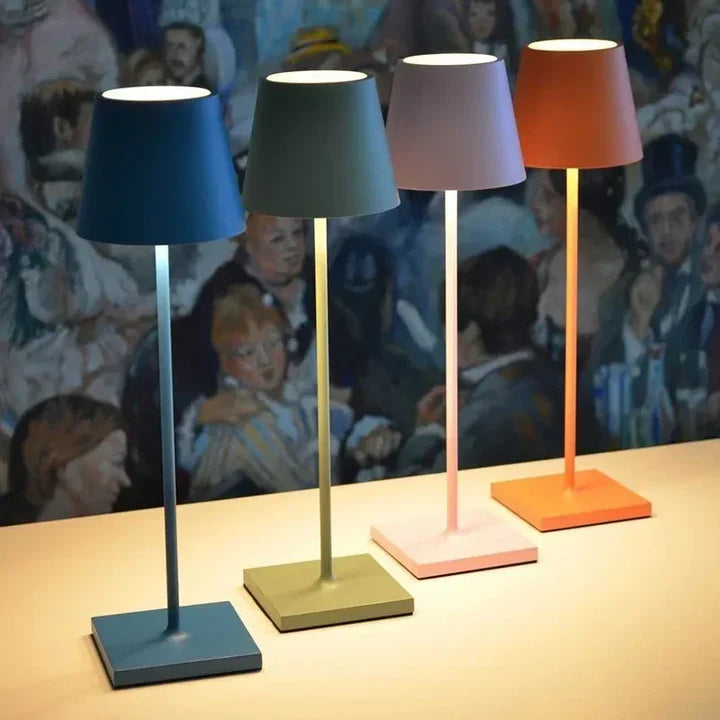Four colorful table lamps on a surface with a painting in the background