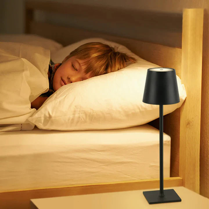 Child sleeping in bed with a black lamp next to them