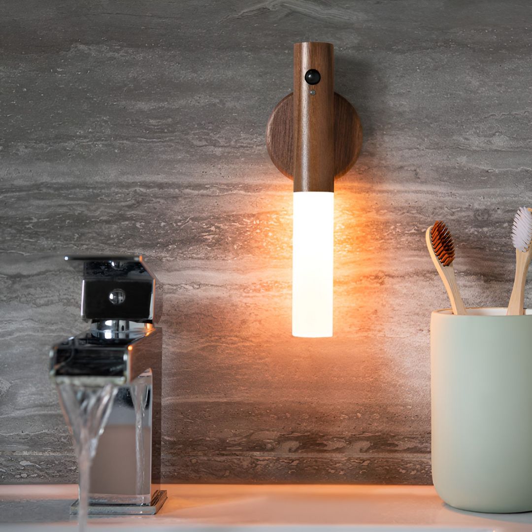 Wooden wall sconce with a light fixture on a bathroom wall, next to a glass container and toothbrush holder.